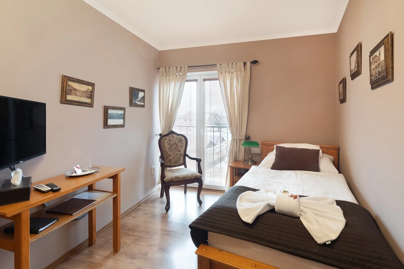 Útulný jednolůžkový pokoj s balkonem a elegantním křeslem.