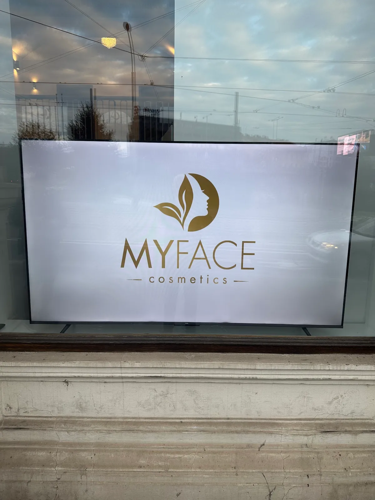 Zlaté logo MYFACE Cosmetics s ženským profilem ve výloze.