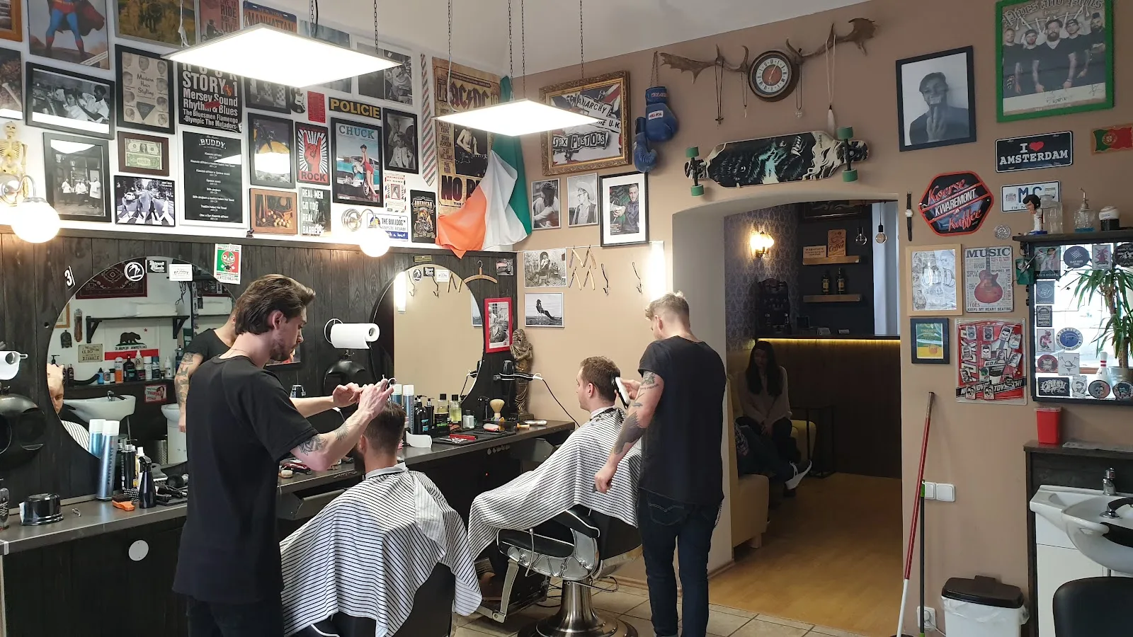 Barbershop s holiči stříhajícími vlasy, plný zarámovaných obrázků.