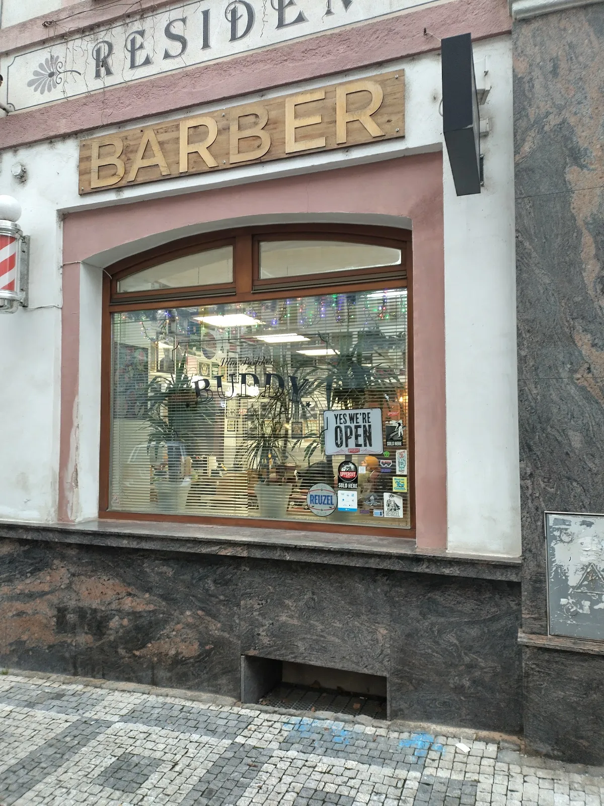 Vnější pohled na holičství BUDDY s cedulí BARBER.