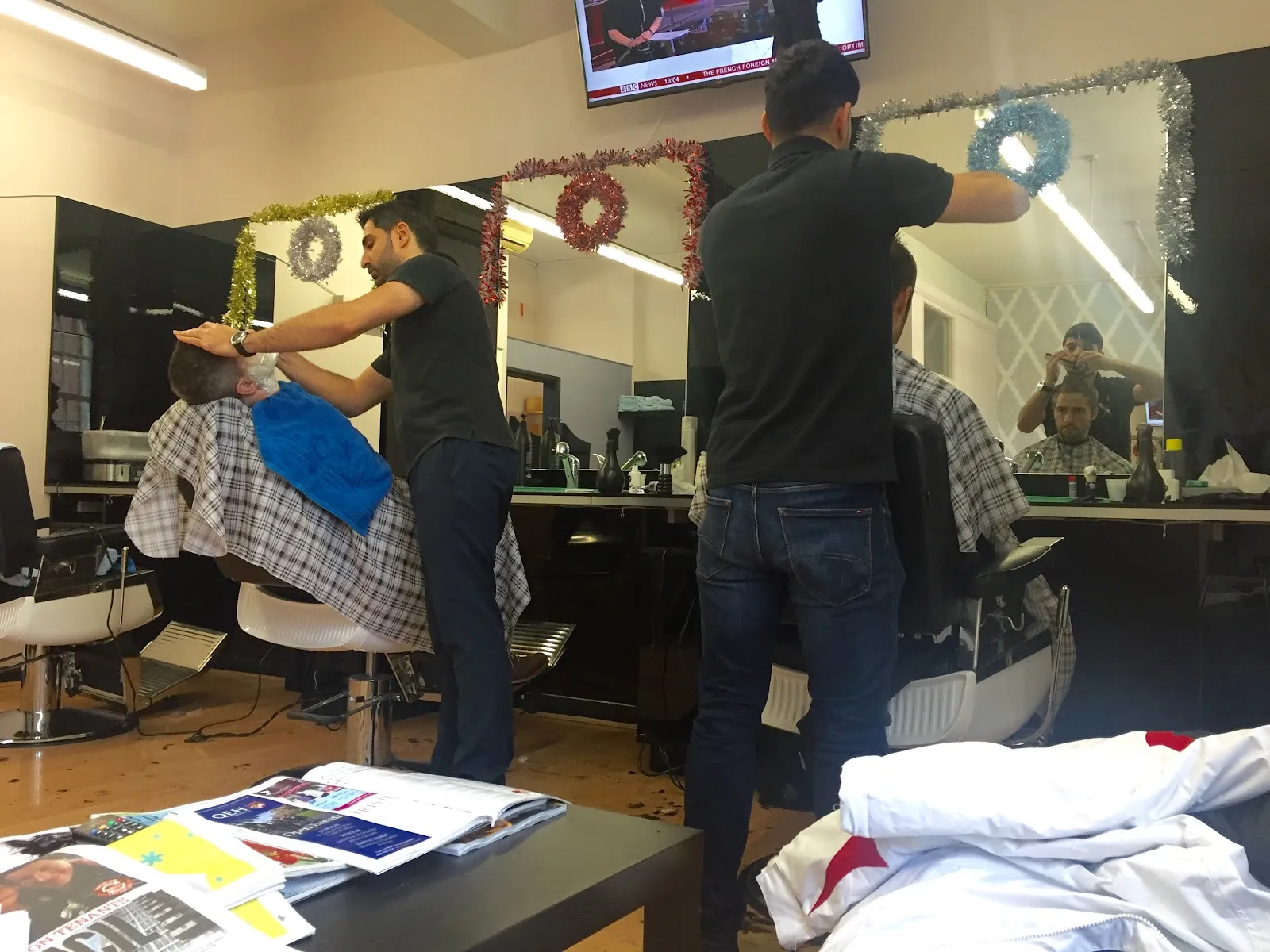 Barbers attending clients amidst festive holiday tinsel decorations.